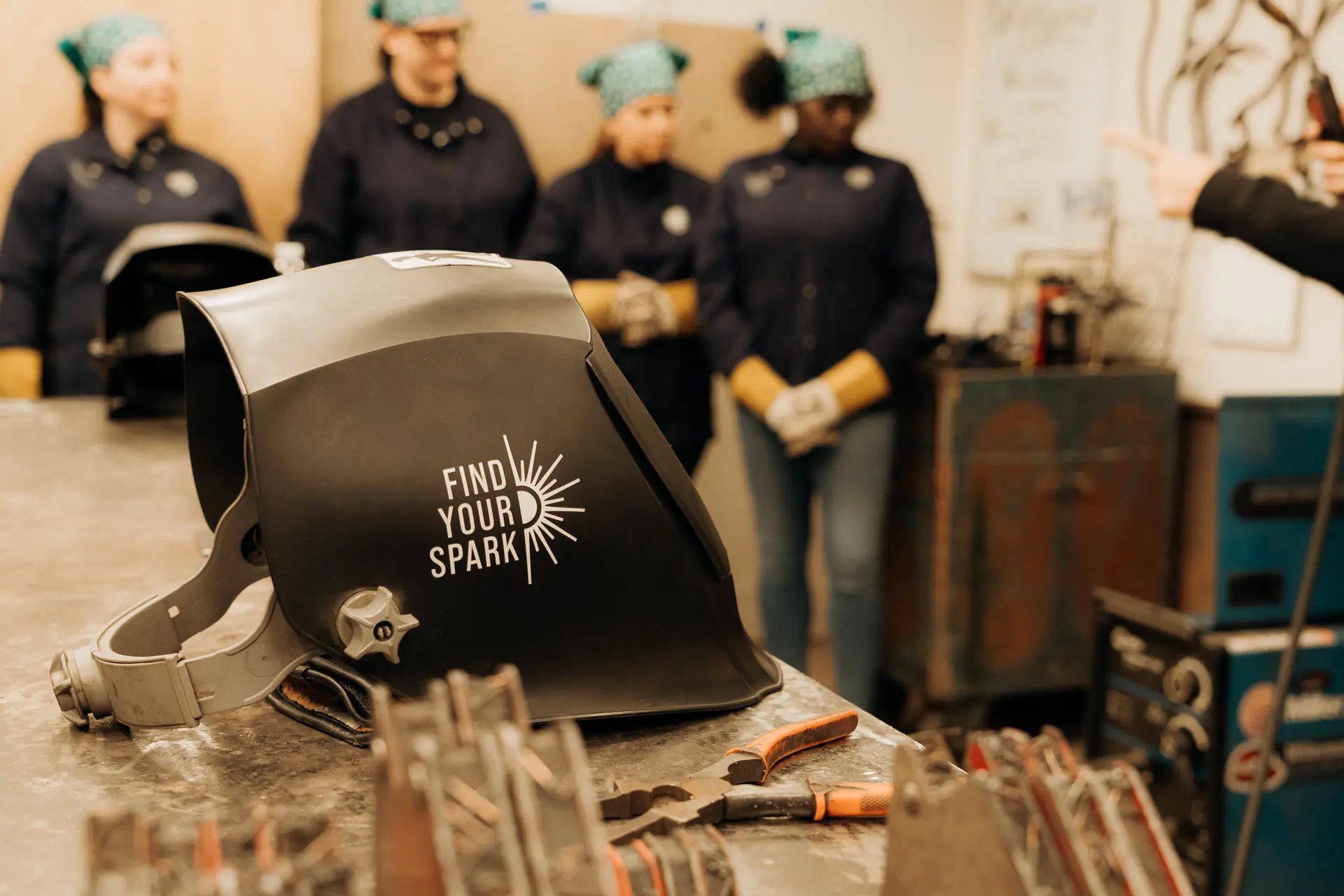 A Find Your Spark welding helmet resting on the bench as participants look on
