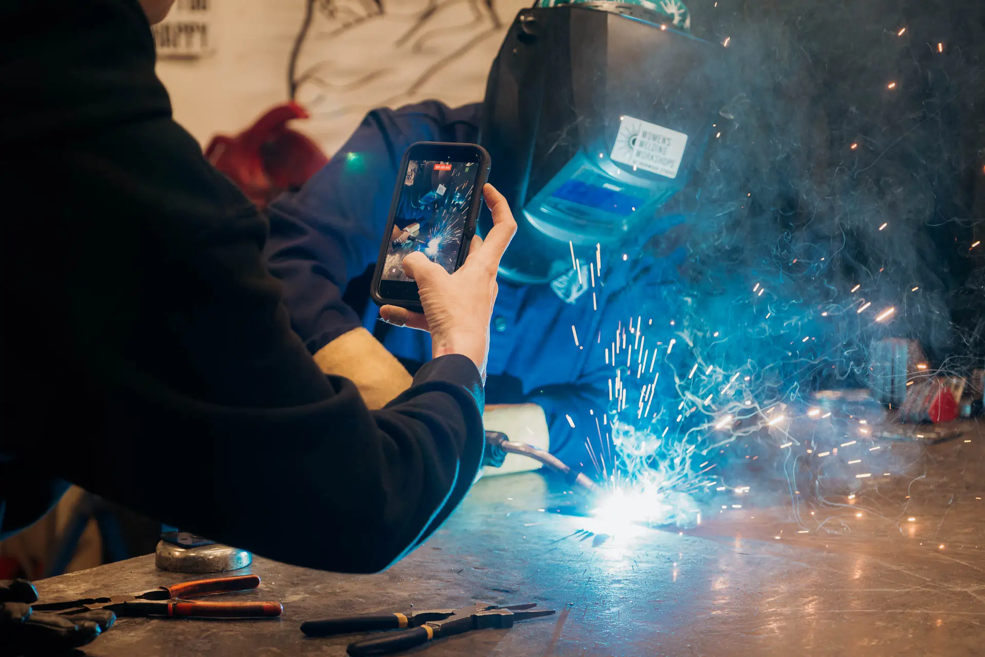 A participant filming bright blue welding sparks on a phone